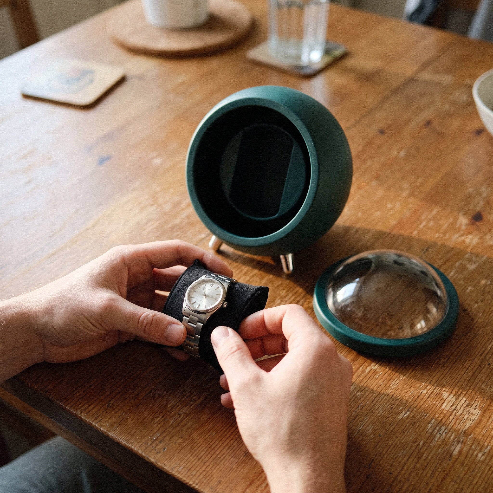 Hands settling a watch on its cushion beside a Green winder